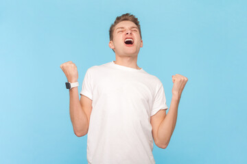 Portrait of extremely happy cheerful man wearing white t-shirt celebrating his achievements and...