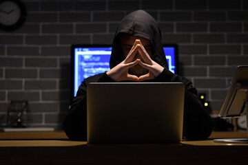 Thoughtful hacker with laptop at table in dark room