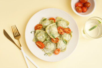 Plate of tasty ravioli and glass with water on yellow background