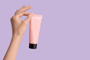 Female hand with tube of natural cream on lilac background, closeup