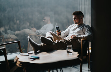 Modern lifestyle image depicting a leisure moment with a man unwinding on chair while browsing his...