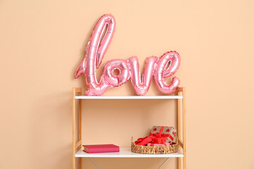 Bookshelf with word LOVE made from balloons and gift boxes near beige wall. Valentine's Day celebration