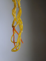 close up of yellow rubber band hanging in blurry room. dangling woven rubber. rubber bracelet
