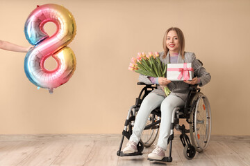 Young woman in wheelchair with tulips, gift and balloon on beige background. International Women's Day