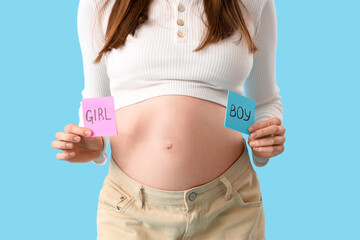 Beautiful pregnant woman holding papers with gender on blue background, closeup