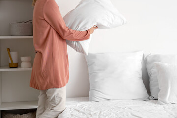 Woman putting pillow on bed in light bedroom - obrazy, fototapety, plakaty