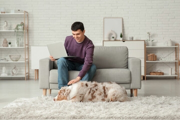 Young man with Australian Shepherd dog and laptop at home