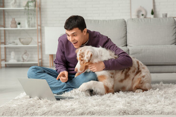 Young man with Australian Shepherd dog and laptop at home