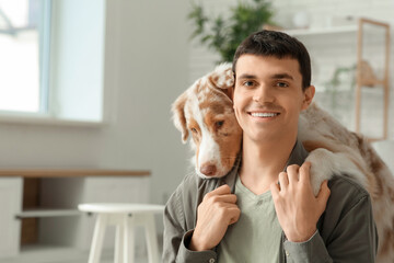 Young man with cute Australian Shepherd dog hugging at home, closeup