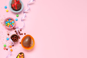 Paper cups with sweet chocolate Easter eggs and candies on pink background