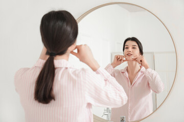 Beautiful young woman doing face building exercise near mirror in bathroom