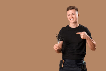 Young barber pointing at scissors on brown background