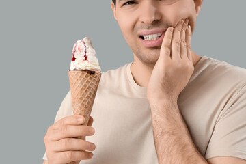 Young man with ice cream suffering from toothache on light background, closeup