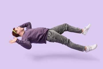 Joyful young man with sunglasses flying on lilac background