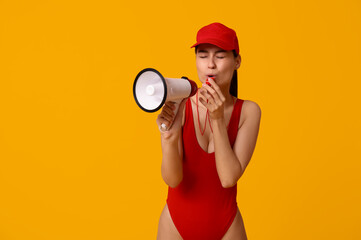 Female lifeguard with megaphone blowing in whistle on yellow background