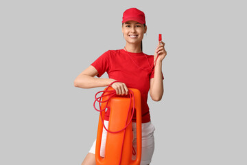 Female lifeguard with rescue tube buoy and whistle on grey background