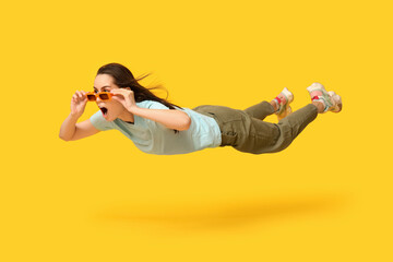 Surprised young woman in sunglasses flying on yellow background