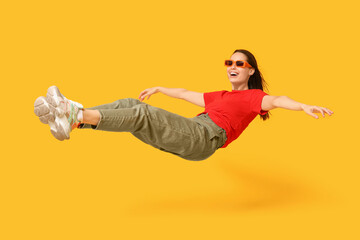 Fototapeta na wymiar Joyful young woman in sunglasses flying on yellow background