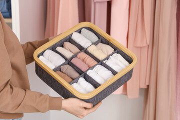 Beautiful young woman with clean clothes in organizer at wardrobe, closeup