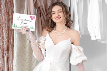 Beautiful young happy woman holding card with text INVITATION FOR PROM  in wardrobe