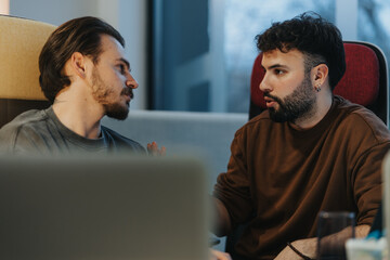 An intimate and focused shot of two men having a serious discussion indoors. Natural light bathes...