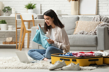 Young woman with blue t-shirt and laptop sitting near suitcase in living room