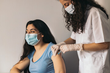 doctor makes vaccination to young woman with surgical mask - obrazy, fototapety, plakaty