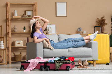 Happy woman with hat lying on sofa near suitcases in modern living room