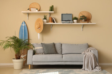 Interior of light living room with cozy sofa, surfboard, houseplant and shelves