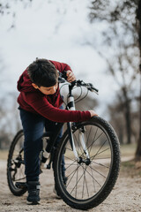 A young boy in casual wear is riding his bicycle in the park, enjoying the leisure and freedom of outdoor activities. - obrazy, fototapety, plakaty