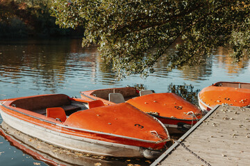 Several boats with oars are moored at the water's edge at the pier in the city park for water walks on the river, lake or pond. Sunset.
