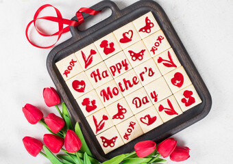 Mothers Day. Modern square shortbread cookies with marmalade filling in a themed form, mother's day, moms, flower, butterfly, mother and child, hearts. On a wooden plate. With red tulips. Top view