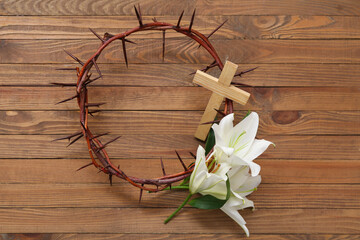 Crown of thorns with white lilies and cross on wooden background