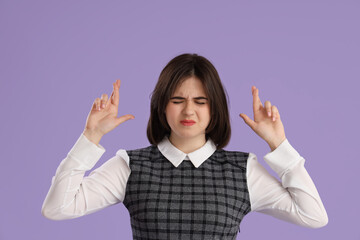 Beautiful young stressed businesswoman with crossed fingers on purple background. Stress Awareness Month - obrazy, fototapety, plakaty