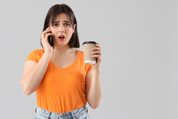 Young stressed woman with cup of coffee talking by mobile phone on grey background. Stress Awareness Month - obrazy, fototapety, plakaty
