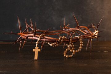 Crown of thorns and beads with cross on wooden table against black grunge background, closeup. Good...