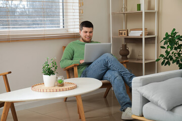 Young man sitting on chair and using laptop in living room