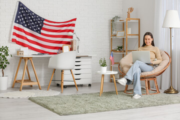 Young woman using laptop in room with USA flag on wall