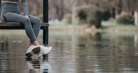 A serene moment as a fit woman sits on a pier, reflecting by the calm waters of a peaceful lake.