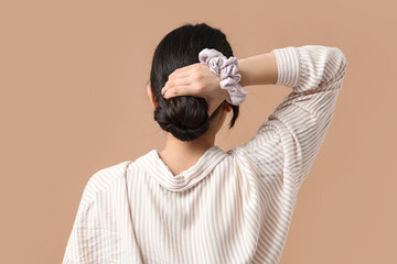 Woman with bun hairstyle and silk scrunchy on beige background, back view