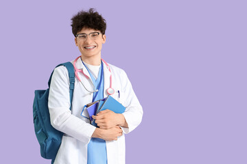 Male medical intern with notebooks on lilac background