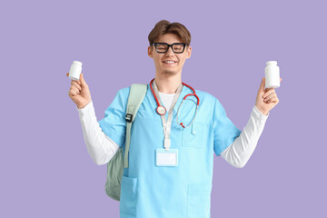 Male medical intern with pill bottles on lilac background