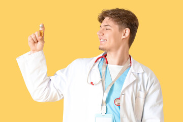 Male medical intern with ampule on yellow background