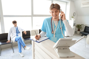 Male medical intern talking by telephone at reception in clinic