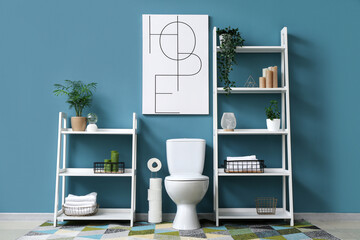 Interior of blue bathroom with toilet bowl, shelving units and picture