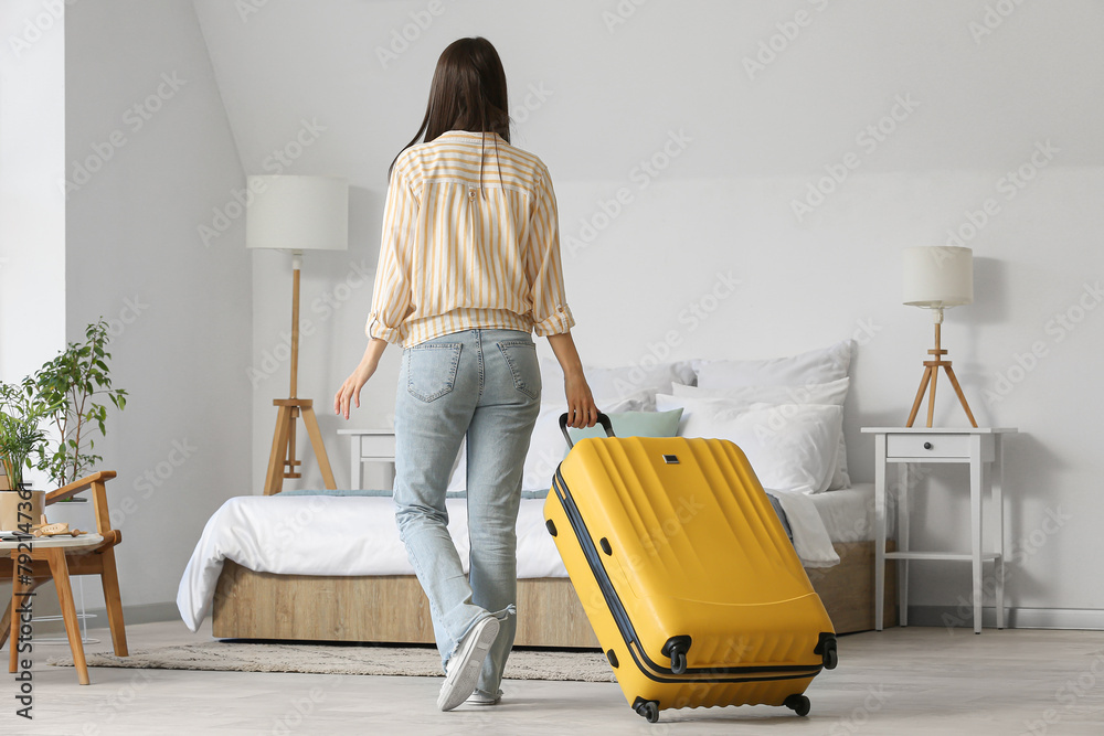 Poster woman with suitcase in light hotel room, back view