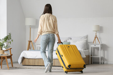 Woman with suitcase in light hotel room, back view - obrazy, fototapety, plakaty