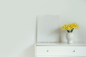 Vase with daffodils and painting on commode in light room