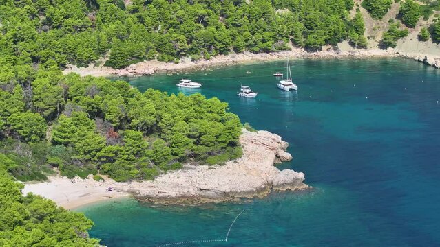 AERIAL: A scenic shot of a secluded bay in the remote part of the Hvar island. A tiny hidden beach with a few visitors with a small bay with a couple of anchored boats nearby, with people relaxing.