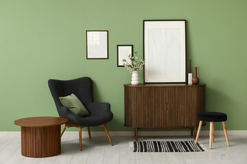 Empty frame and blooming branches on wooden chest of drawers near green wall